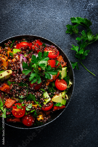 Quinoa tabbouleh salad with tomatoes, paprika, avocado, cucumbers, onion and parsley. Traditional Middle Eastern and Arabic dish. Black kitchen table background, top view