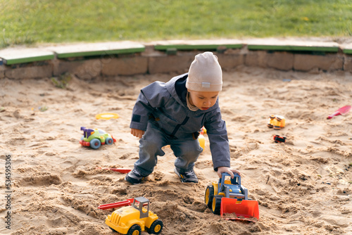 Child playing with toys in sandbox. Little boy having fun on playground in sandpit. Outdoor creative activities for kids. Autumn, fall and childhood concept © velishchuk