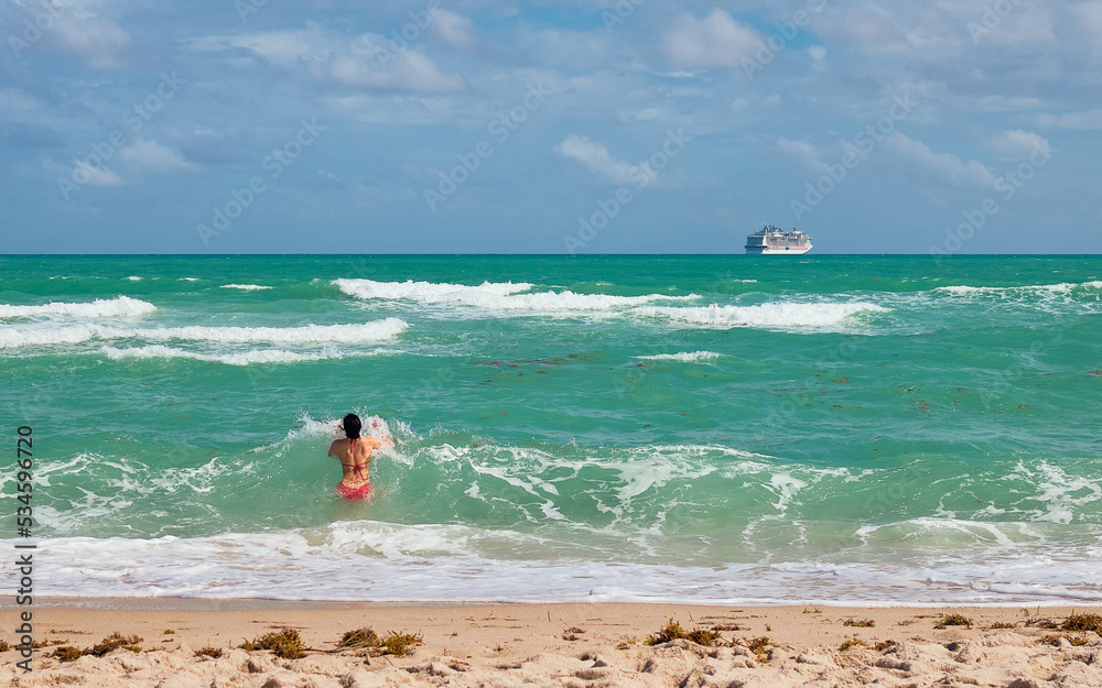 A woman in red bathing suit dives into the ocean as a cruise ship sails away in the distance. A woman in red bathing suit dives into the ocean as a cruise ship sails away in the distance.
