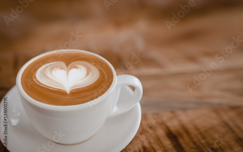 Cappuccino cup with latte art heart on wooden table.