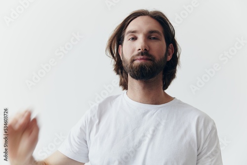 Portrait of a sad man with a black thick beard and long hair in a white t-shirt on a white isolated background