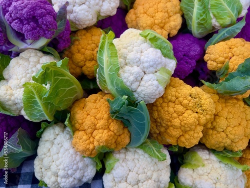 Papier peint Whole heads of white, orange, and purple raw cauliflower with green leaves piled