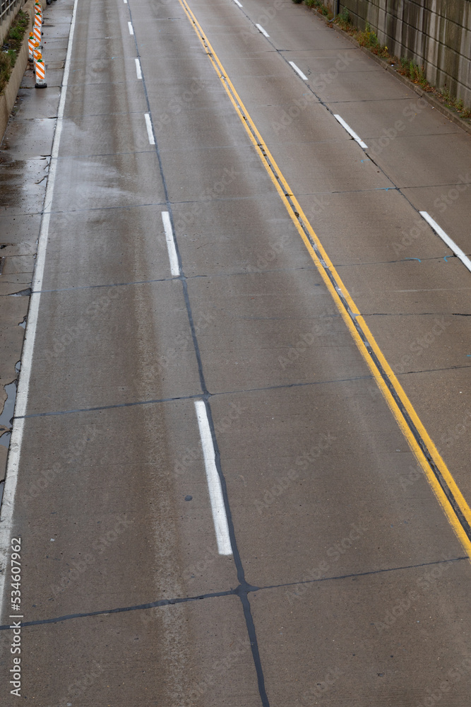 Overhead view of a four lane road bounded by walls, wet with rain, vertical aspect