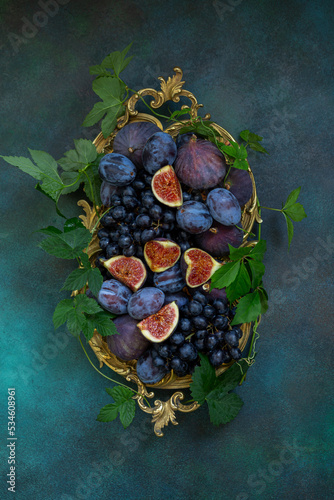 Fresh fruits figs, grapes and plums on a vintage dish on a blue background. Top view