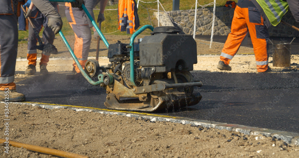 Construction worker using vibration compactor for laying asphalt surface at yard