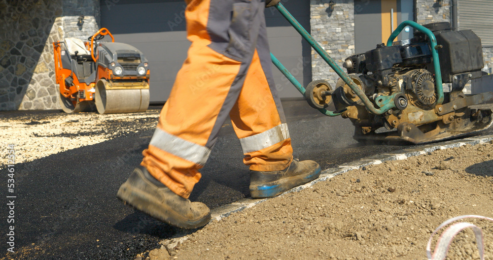 Rear view of worker using vibration compactor for smoothing asphalt surface Rear view of worker using vibration compactor for smoothing asphalt surface