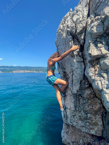 CLOSE UP: Female climber deep water solo climbing above clear blue seawater
