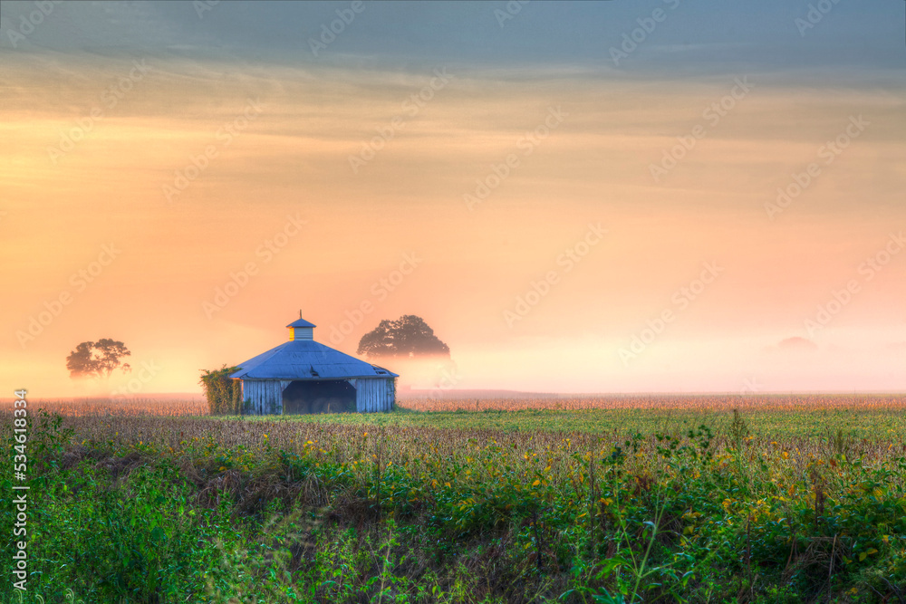 Barn between the trees  Highway 94 in Warren County at dawn, the colorful sunlight dances on the low lying fog. 