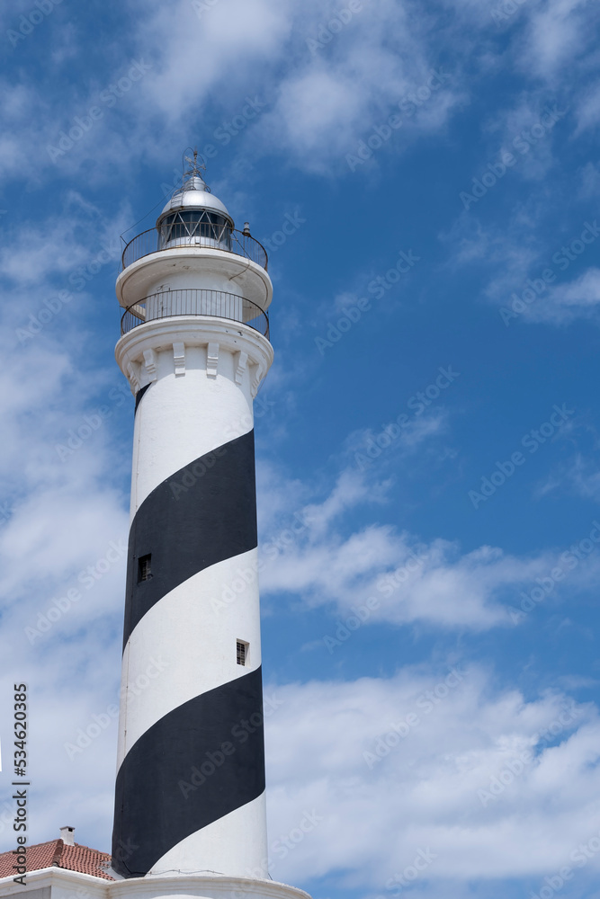 Favaritx lighthouse with its tower painted with a blue and white spiral, with the sky of cotton clouds, low point of view, copy space, vertical