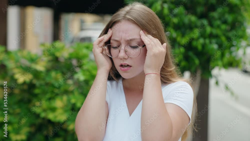 Young blonde woman suffering headache standing at street Young blonde woman suffering headache standing at street