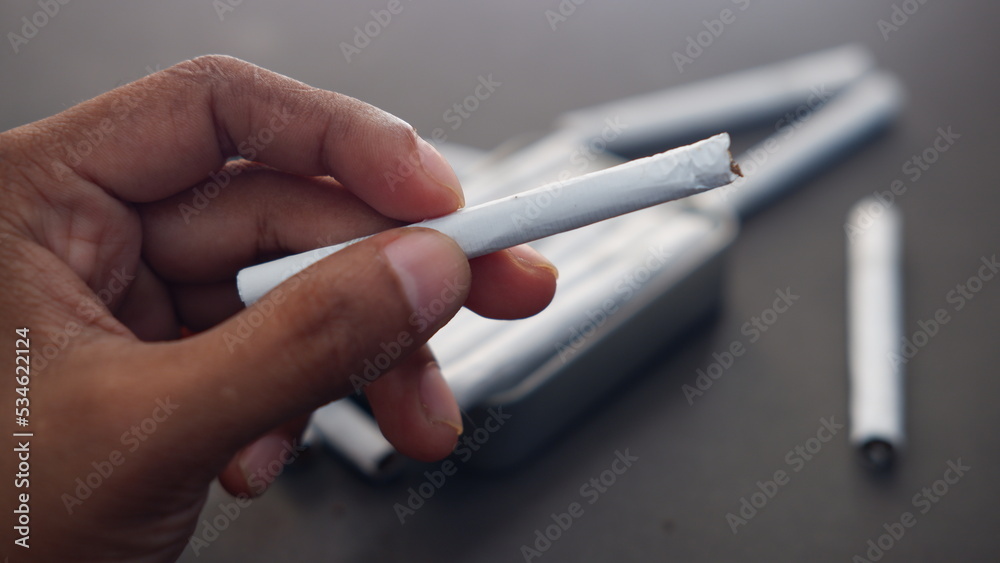 Man hand holding a cigarette, weed, ganja, marijuana. Unhealthy lifestyle concept Man hand holding a cigarette, weed, ganja, marijuana. Unhealthy lifestyle concept