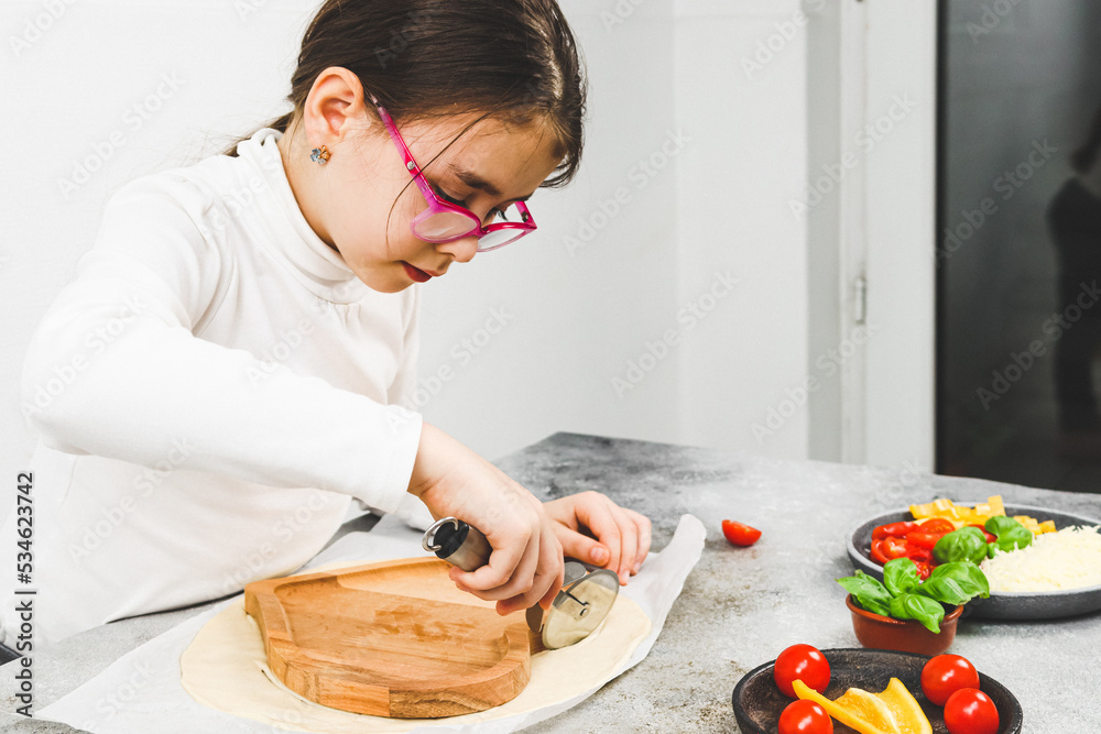 Caucasian girl in a white turtleneck cuts dough on a wooden plate with a metal scabbard. Caucasian girl in a white turtleneck cuts dough on a wooden plate with a metal scabbard.