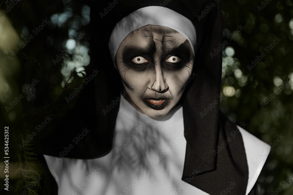 Portrait of scary devilish nun near tree outdoors. Halloween party look Portrait of scary devilish nun near tree outdoors. Halloween party look