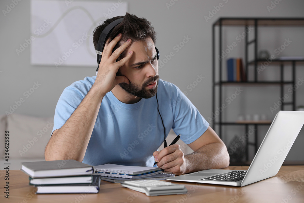 Confused young man watching webinar at table in room Confused young man watching webinar at table in room