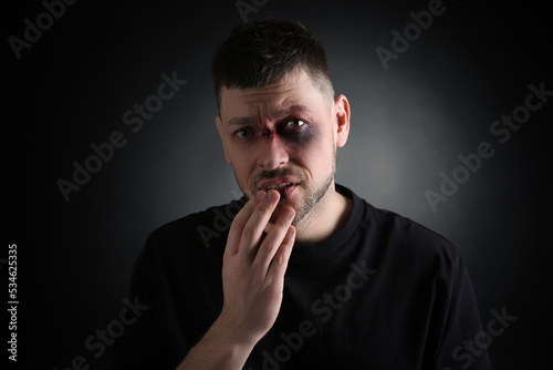Man with facial injuries on dark background. Domestic violence victim
