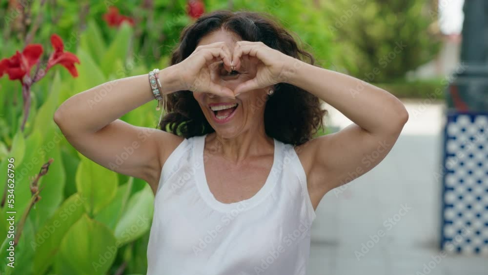 Middle age woman smiling confident doing heart gesture with hands at park Middle age woman smiling confident doing heart gesture with hands at park
