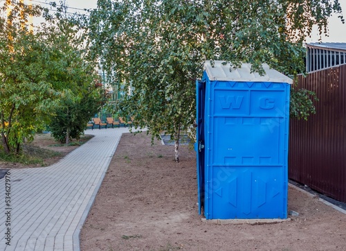 A blue outdoor toilet stands near the sidewalk on the ground