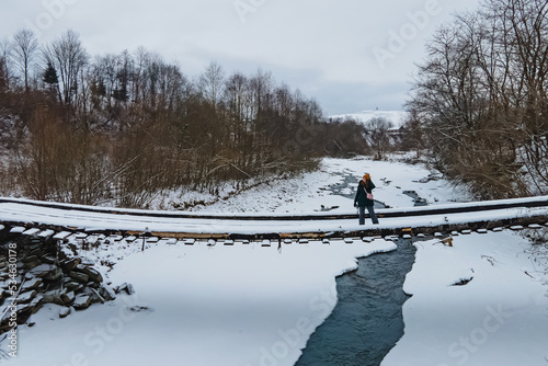 Woman on the small bridge over the frozen river in winter