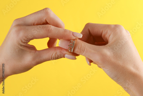 Golden ring in the form of crown with diamonds on female finger. Yellow background