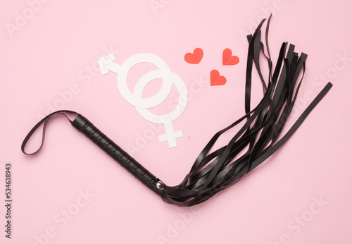 Leather whip from a sex shop, gender symbols with hearts on a pink background. Sex, love games
