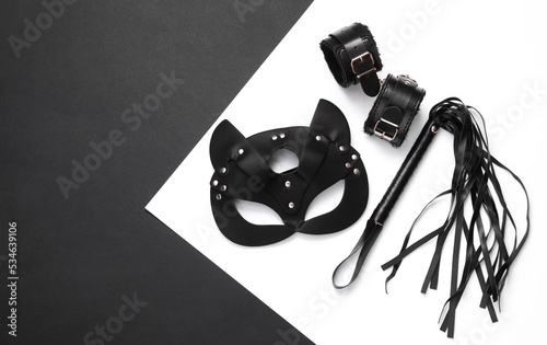 Sex shop toys. Leather whip, cat mask and handcuffs on a black white background. Top view photo