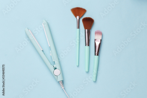 Hair iron with make-up brushes on a blue background. Top view. Flat lay