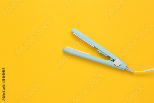 Mini hair straightener on yellow background. Top view