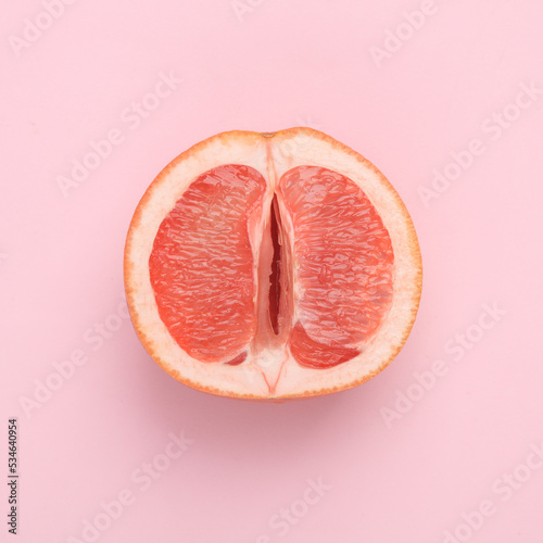 Gynecology, female intimate hygiene. Half of a ripe grapefruit symbolizing the female vagina on a pink background. Creative idea, allegory, fresh idea. Top view photo