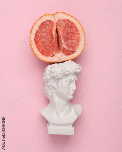 David bust and half of grapefruit symbolizing the female vagina on a pink background