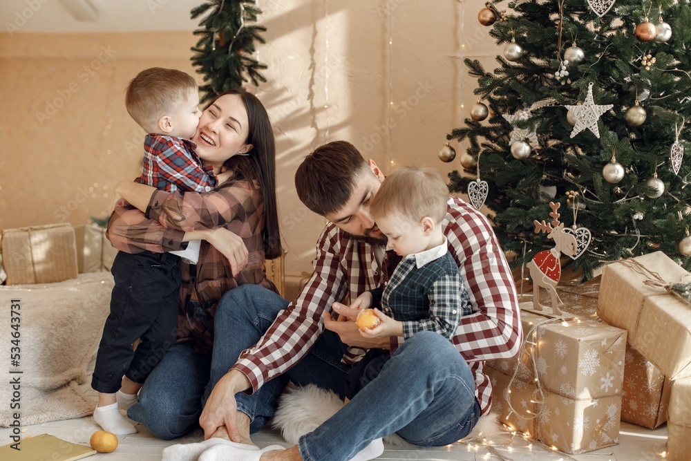 Young family in plaid shirts sitting near Christmas tree