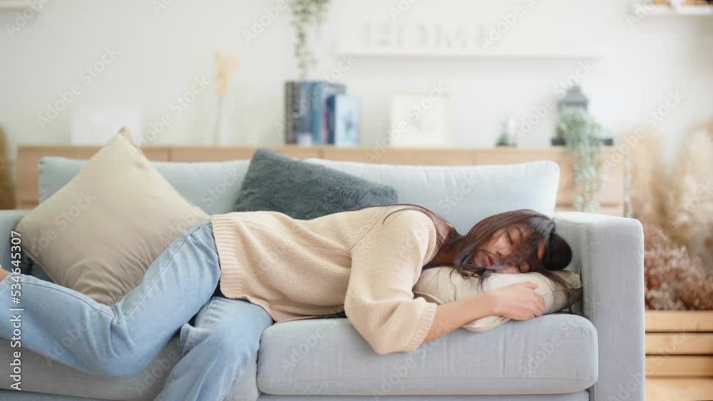 Asian woman resting at home on couch, feeling exhausted after work, lacking energy, or overworked, too tired, and lacking motivation Asian woman resting at home on couch, feeling exhausted after work, lacking energy, or overworked, too tired, and lacking motivation