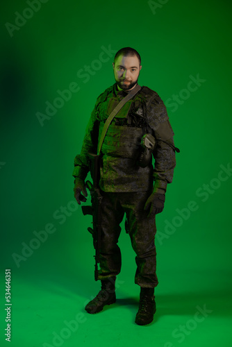 soldier in the studio on a green background with colored light. a man in military uniform with a gun, rifle or machine gun. military. airball player