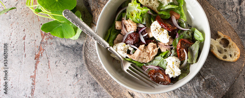 bowl with salad with cod liver, soft cheese and sun-dried plums on the table