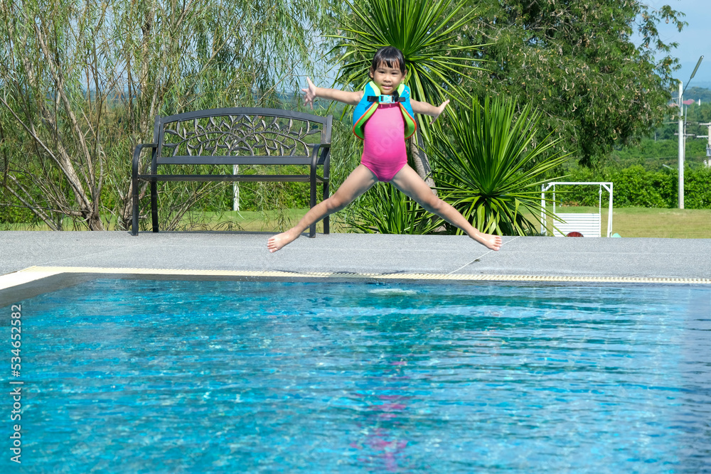 Little girl plays in the outdoor swimming pool of tropical resort during family summer vacation. Kids learning to swim. Healthy Summer Activities for Kids.