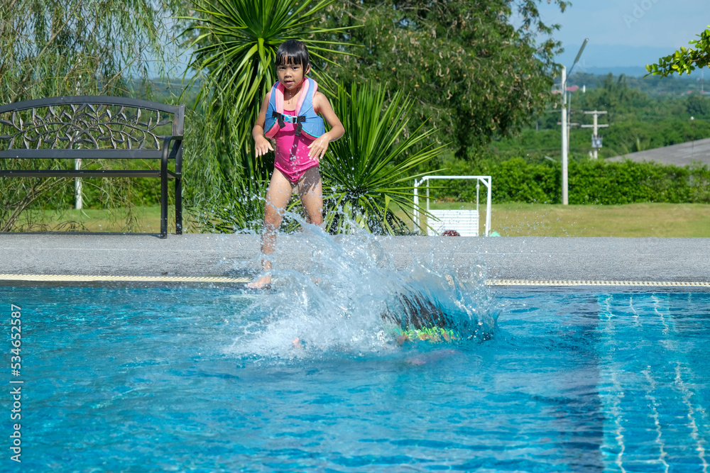 Happy little sisters play in outdoor swimming pool of tropical resort during family summer vacation. Kids learning to swim. Healthy Summer Activities for Kids.