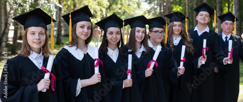 Row of young people in graduation gowns outdoors. Age student. Widescreen.