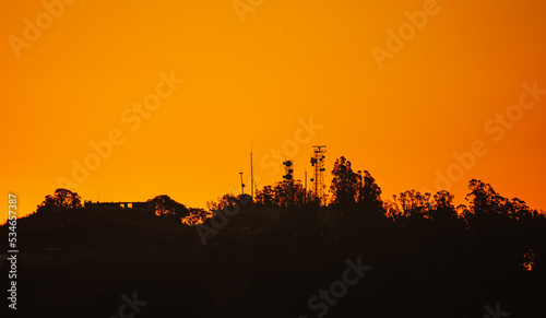 Obraz na płótnie Telecommunication scafolding tower with internet data voice and GSM antennas photographed on top of a hill against amazing orange sunrise sky. Communication technology industry mixed with nature. w salonie