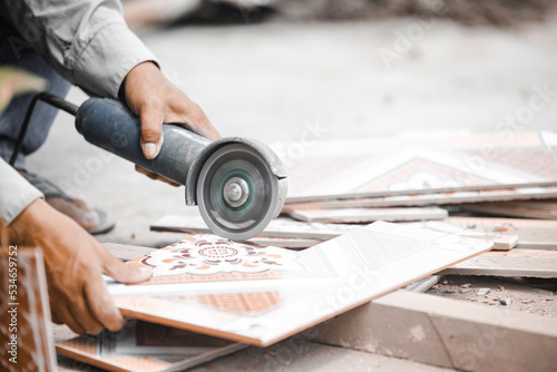 Worker cutting a tile using an angle grinder at construction site. Cutting large ceramic tiles. The worker cuts the tiles with a special tool. Quality photo. construction concept.