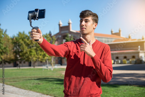 Portrait of businessman recording video presentation at smartphone with steadycam. Focused young man standing outside, holding steadycam while recording video presentation about new object  photo