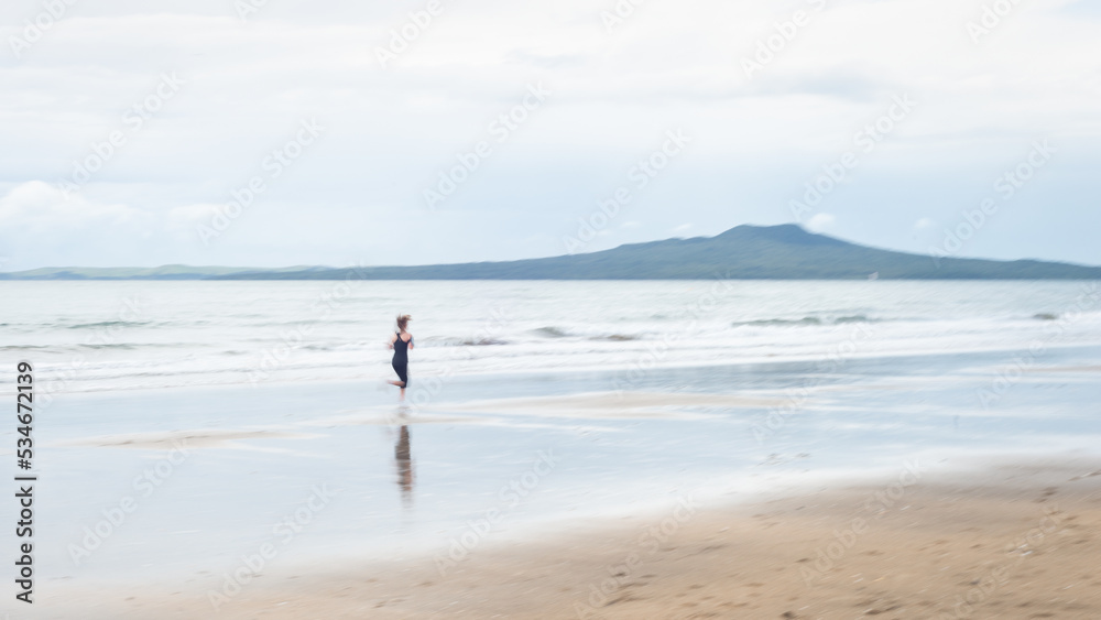 Woman running on Milford beach, Rangitoto Island in the background, Auckland. Image taken using intentional camera movement technique.