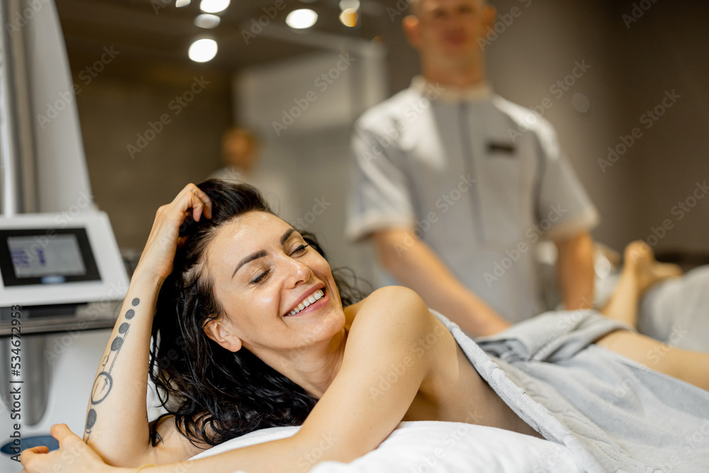Portrait of happy adult woman lying on medical couch during vacuum roller massage procedure at medical beauty centre Portrait of happy adult woman lying on medical couch during vacuum roller massage procedure at medical beauty centre