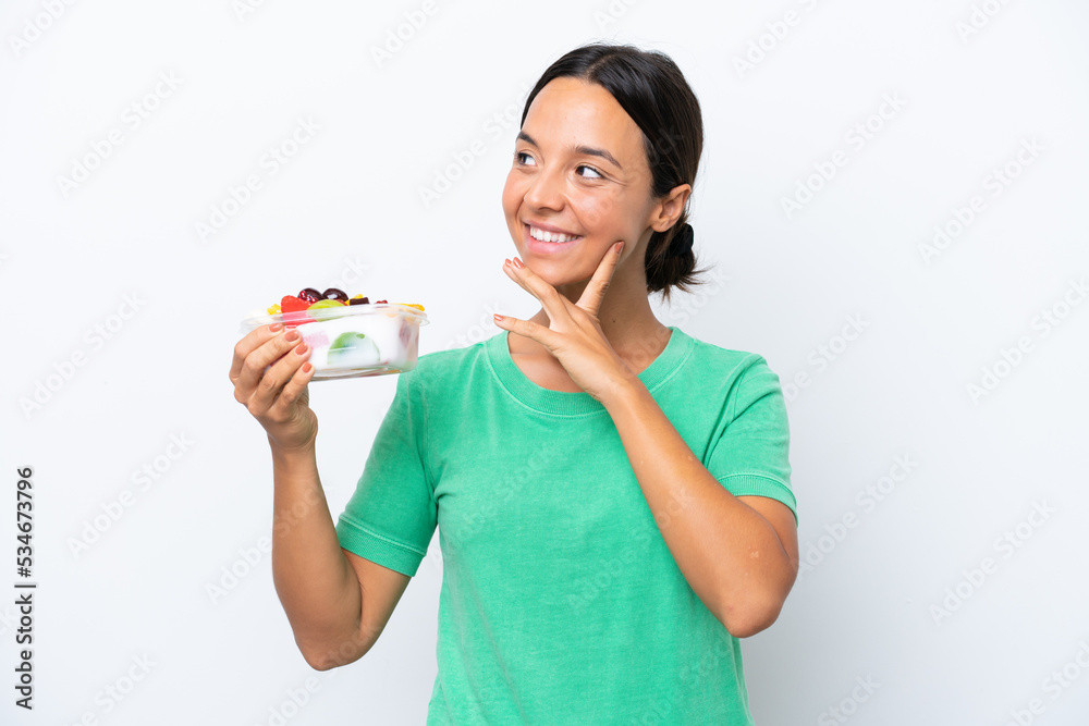 Young hispanic woman holding a bowl of fruit isolated on white background thinking an idea while looking up Young hispanic woman holding a bowl of fruit isolated on white background thinking an idea while looking up