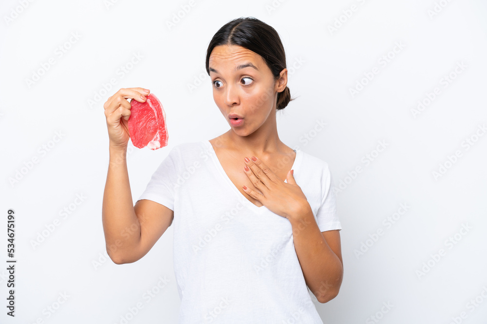 Young hispanic woman holding a piece of meat isolated on white background with surprise and shocked facial expression Young hispanic woman holding a piece of meat isolated on white background with surprise and shocked facial expression