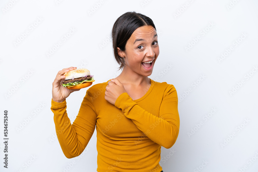 Young hispanic woman holding a burger isolated on white background celebrating a victory Young hispanic woman holding a burger isolated on white background celebrating a victory