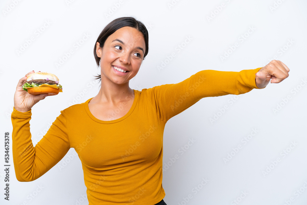 Young hispanic woman holding a burger isolated on white background giving a thumbs up gesture Young hispanic woman holding a burger isolated on white background giving a thumbs up gesture