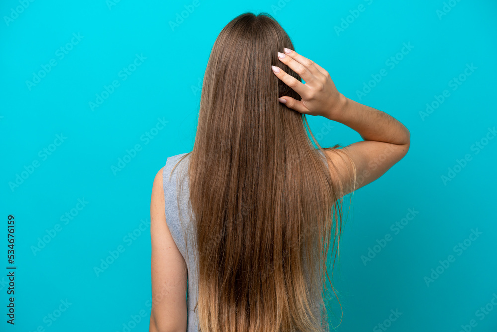 Young Lithuanian woman isolated on blue background in back position and thinking Young Lithuanian woman isolated on blue background in back position and thinking