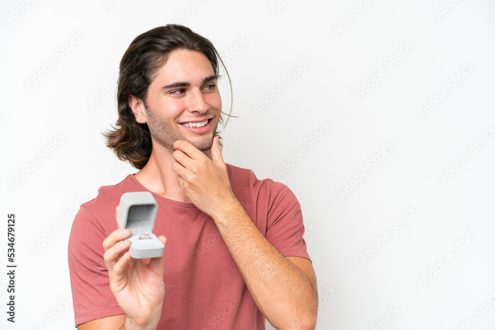 Young handsome man holding a engagement ring isolated on white background thinking an idea and looking side Young handsome man holding a engagement ring isolated on white background thinking an idea and looking side