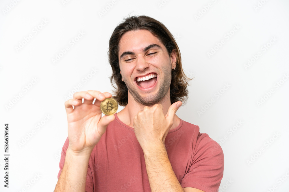 Young handsome man holding a Bitcoin isolated on white background celebrating a victory Young handsome man holding a Bitcoin isolated on white background celebrating a victory