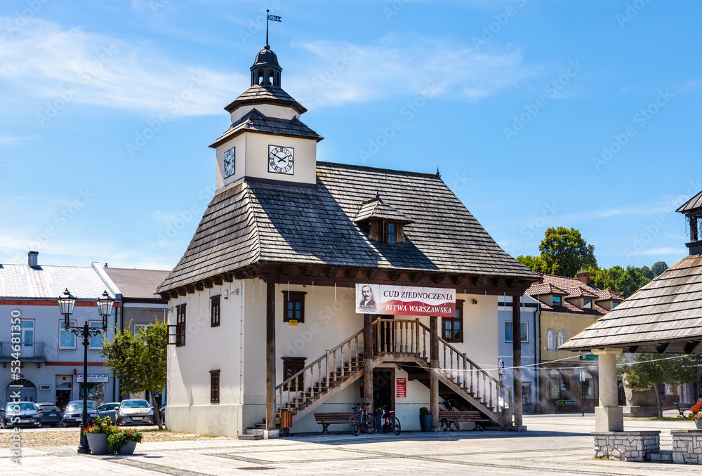 Fototapeta premium Historic Town Hall Ratusz Miejski and renewed wooden well at Rynek Main Market square in old town quarter of Pilica in Silesia region of Poland
