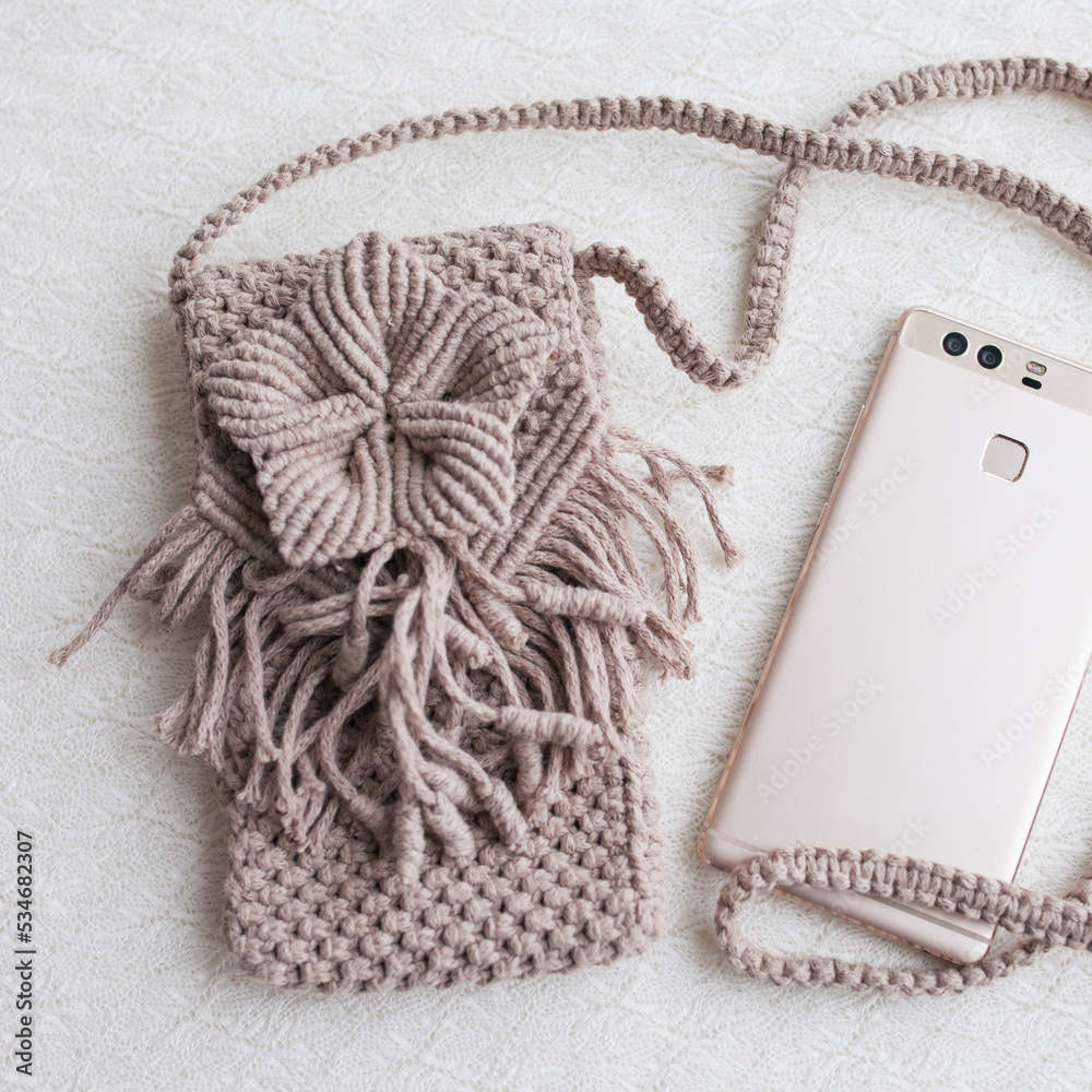 Fototapeta premium Handmade macrame phone bag. ECO friendly natural macrame cotton bag for woman. Hobby knitting handmade macrame. Modern summer concept for woman.